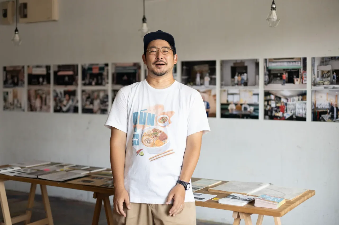 写真家・紺野正瑛氏が展示会場で立っている様子。背後には撮影作品が壁に展示されている。