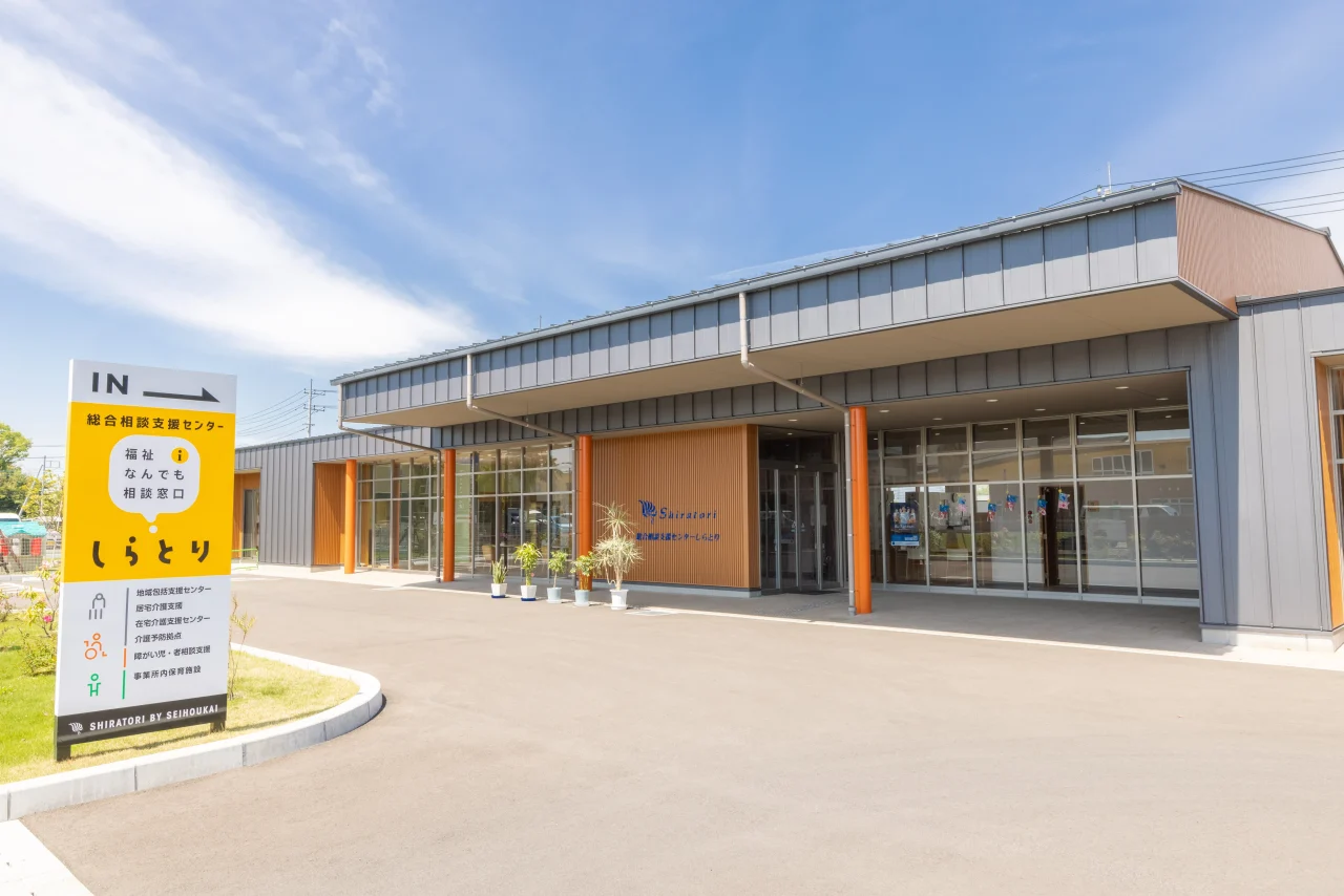 総合相談支援センターしらとりの外観写真。明るい空の下、ガラス張りの建物と案内看板が見える。