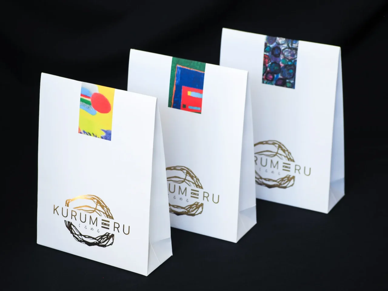 障がいのある利用者が描いたアートをあしらった『KURUMERU』の3種類のパッケージ。