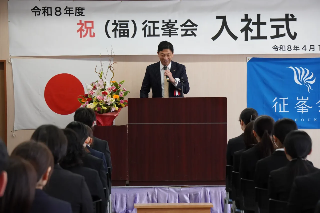 令和8年度 征峯会入社式で登壇する理事長と背筋を伸ばして聞き入る新入職員たち