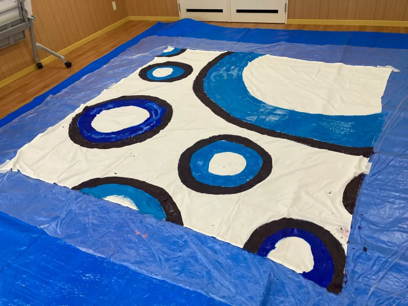 完成した、青や紺色の大小の円と太い曲線が描かれた大きな布のアート作品