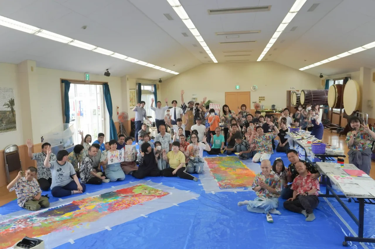 完成した巨大なアート作品を囲み、参加者全員が笑顔で手を振る集合写真