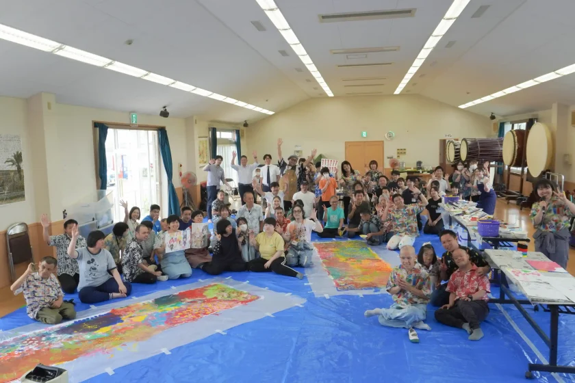 完成した巨大なアート作品を囲み、参加者全員が笑顔で手を振る集合写真
